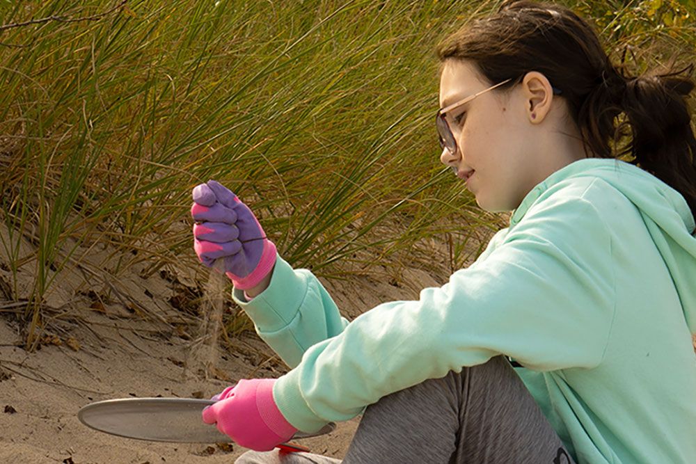 A girl sifts sand along the beach.